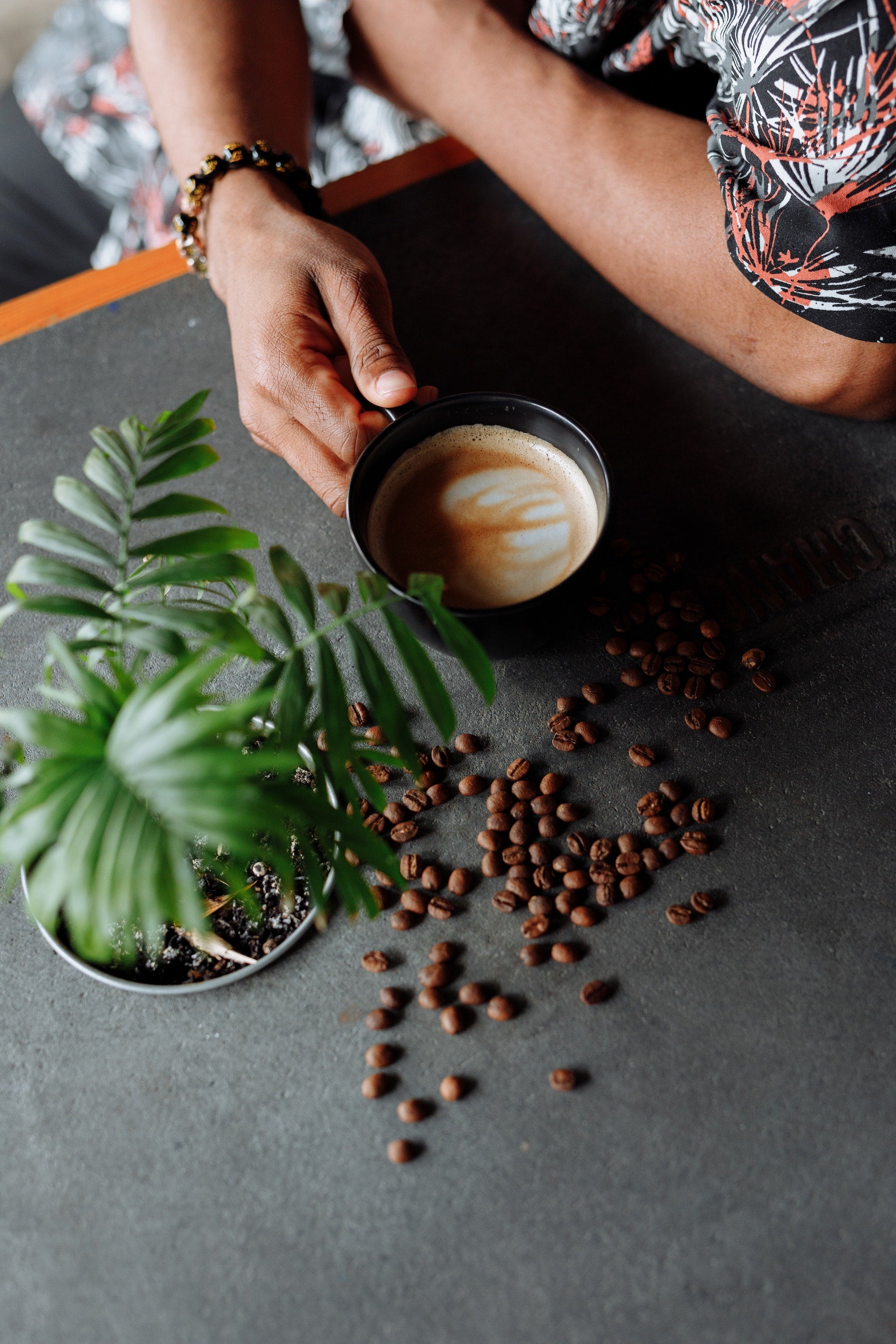 Top-down view of a man holding a cappuccino and coffee beans spilled onto the table